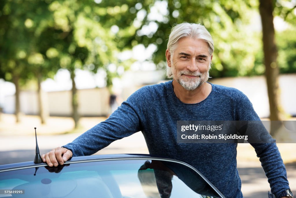 Portrait of mature grey haired Man leaning on car