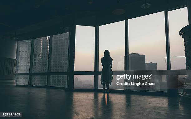 woman looking out the window at city - fensterfront innen stock-fotos und bilder