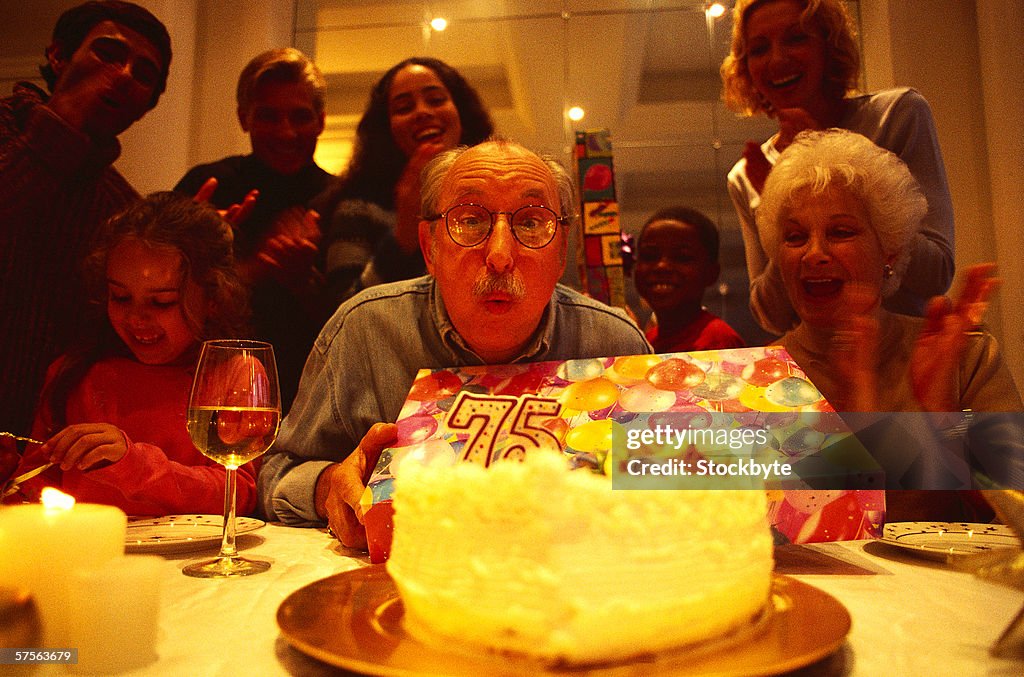 Portrait of an elderly man with a present blowing out candles on a birthday cake