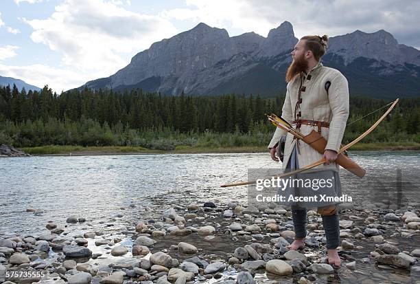 man in viking warrior dress hunts by mtn river - arco frecce foto e immagini stock