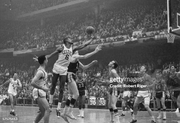 American professional basketball player Bill Russell of the Boston Celtics leaps leaps with arm outstretched to block a shot from an opponent during...