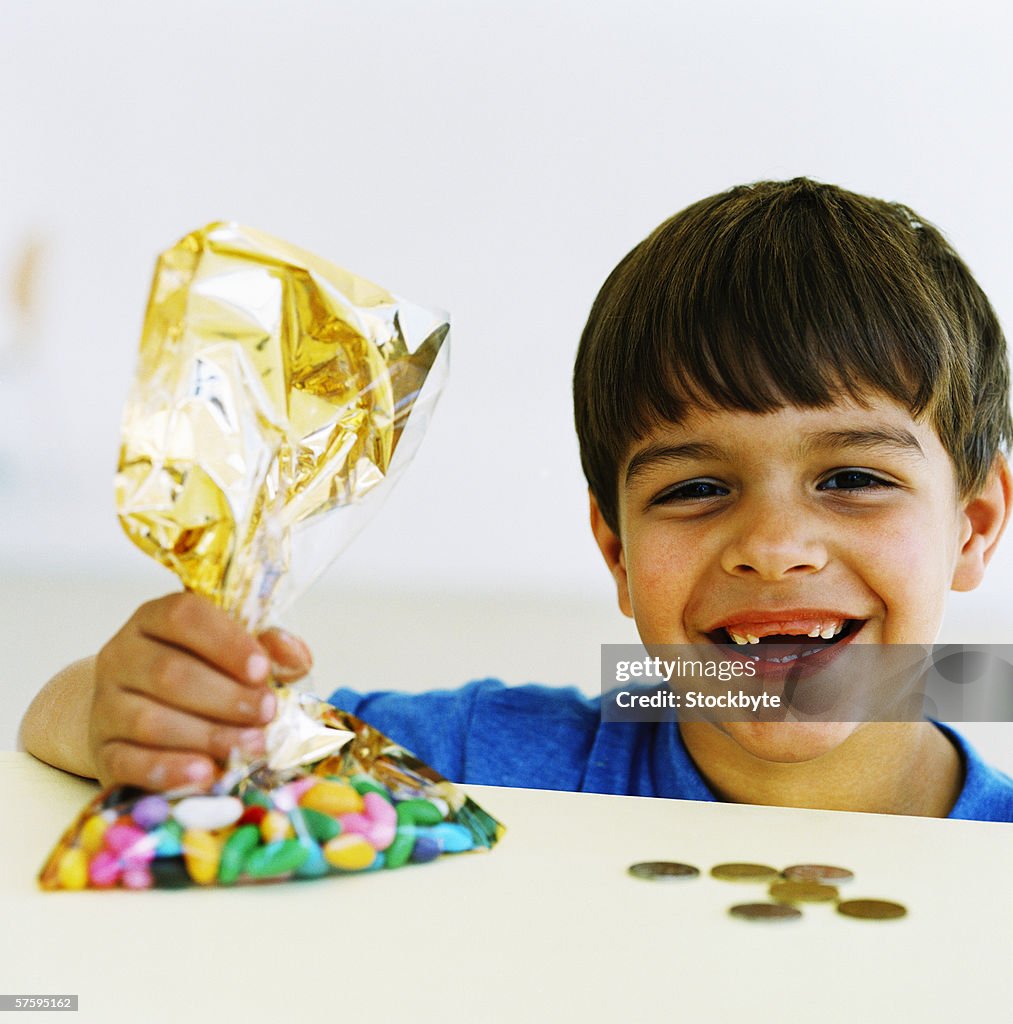 Portrait of a young boy (6-8) laughing holding a bag of candy and money coins on counter in front of him