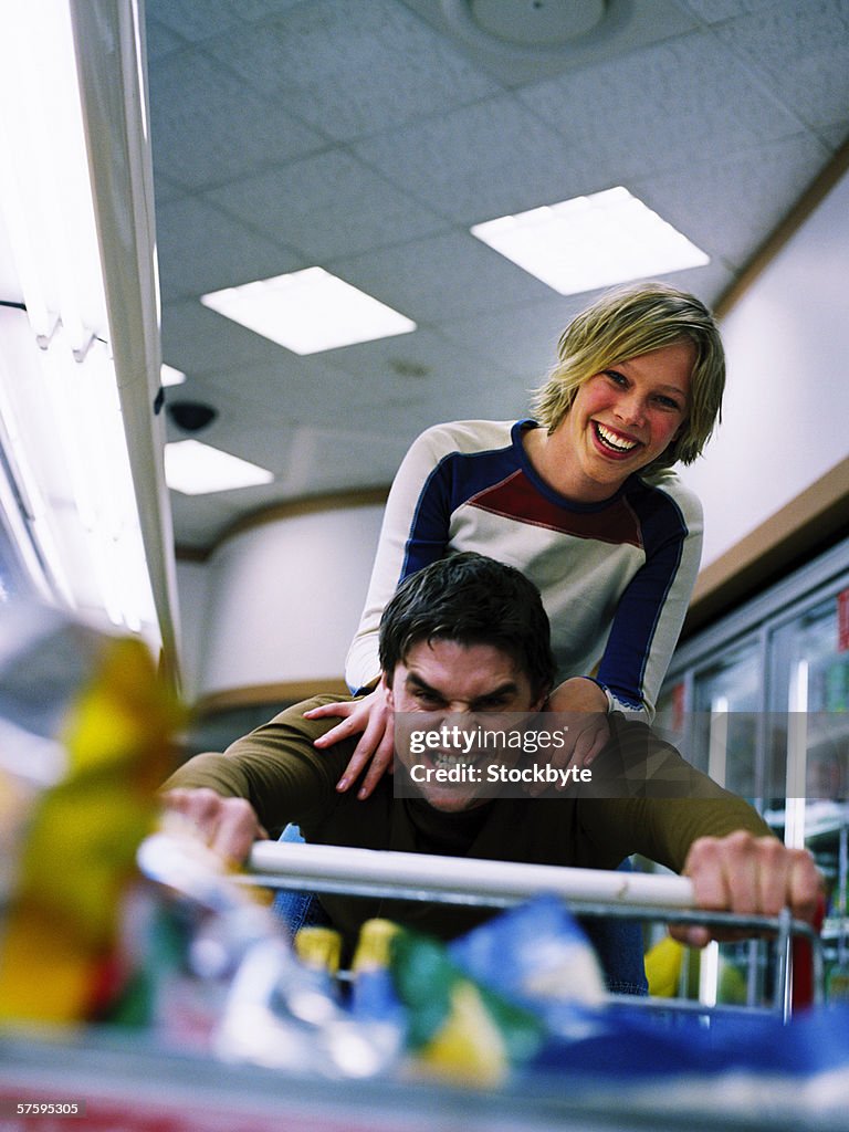 Portrait of a young man pushing a shopping cart with a young woman standing behind him smiling