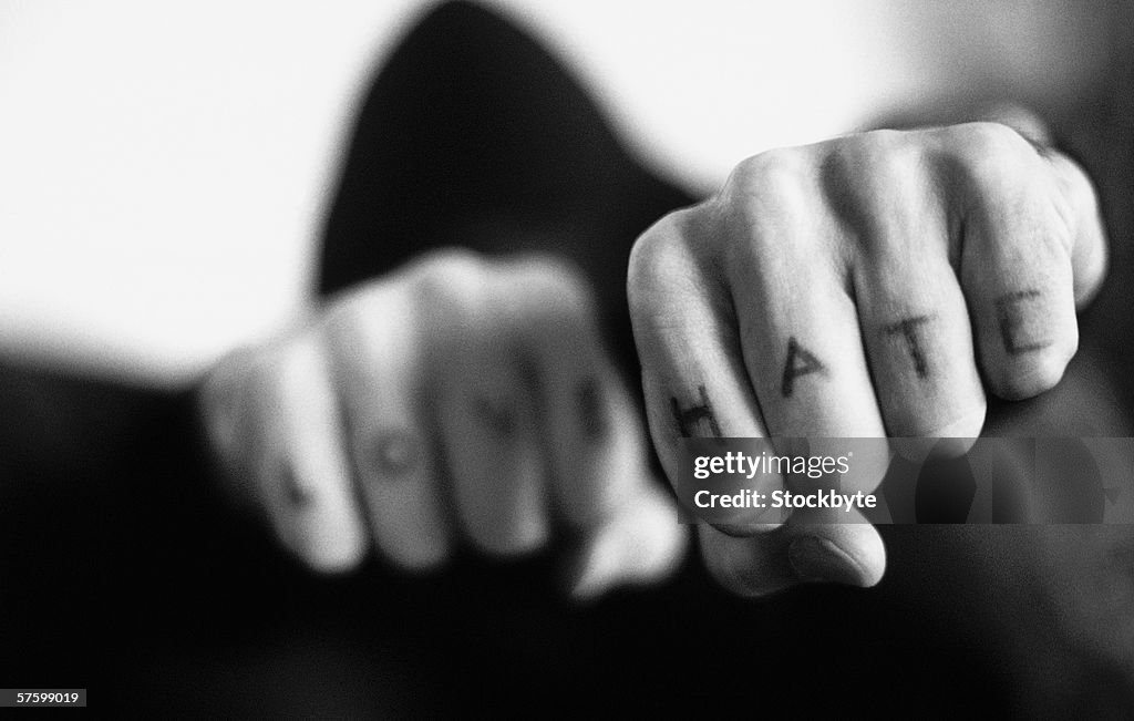 Black and white close-up of fists with love and hate tattooed on the fingers