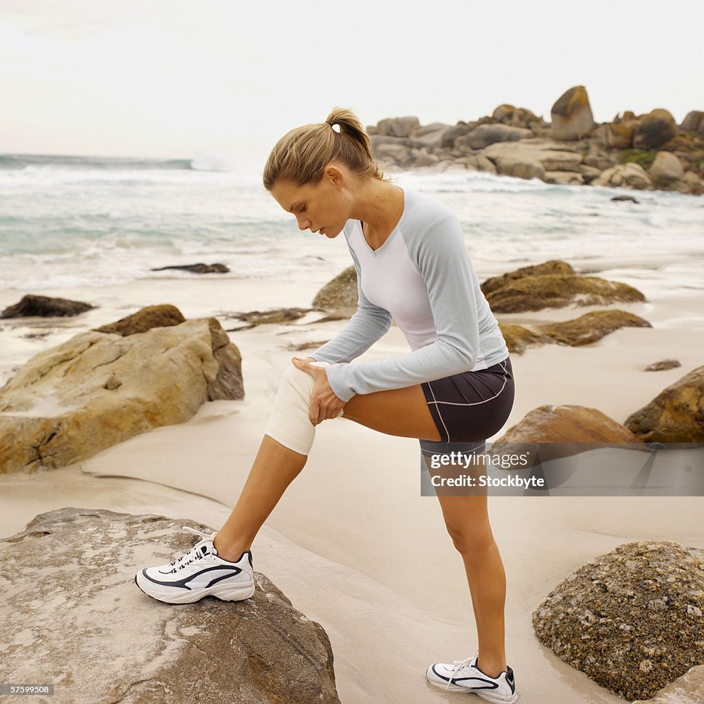 Side view of a concerned woman wearing a knee support holding her knee with her foot on a rock