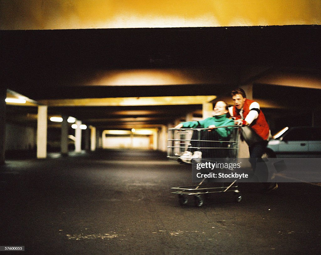 Young man pushing a young woman in a shopping cart