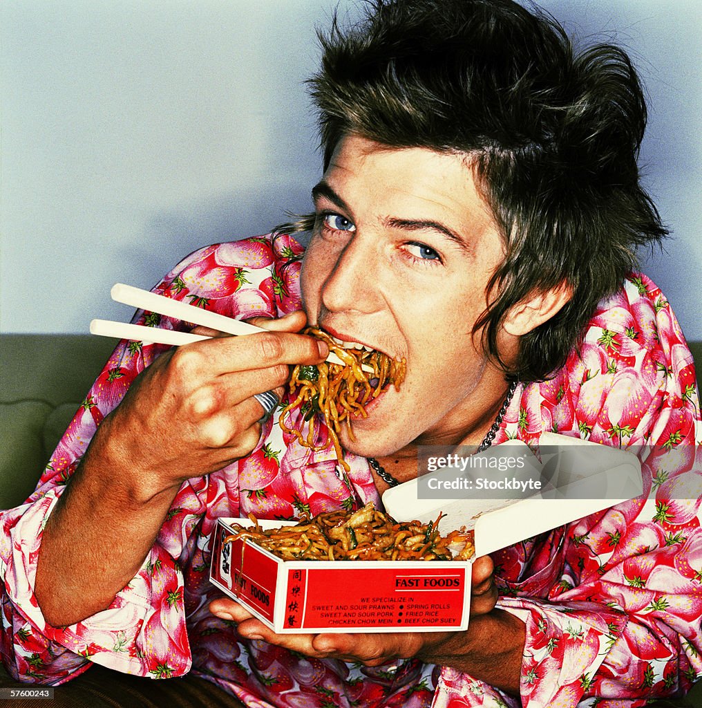 Close-up of a young man eating Chinese food from a box with chopsticks