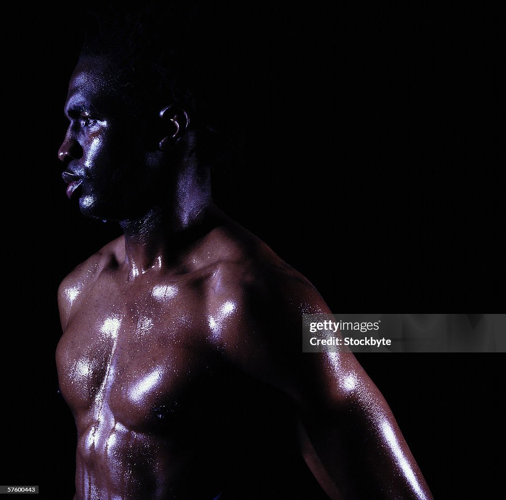 Side profile of a muscular young man covered in sweat