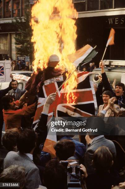 View of demonstrators as they wave Irish flags and burn a British flag in the street, 1980s.