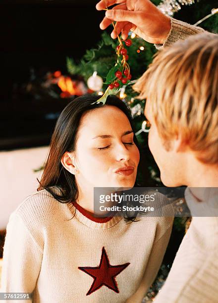 woman waiting to be kissed while a man hangs mistletoe over her head - mistletoe kiss stockfoto's en -beelden