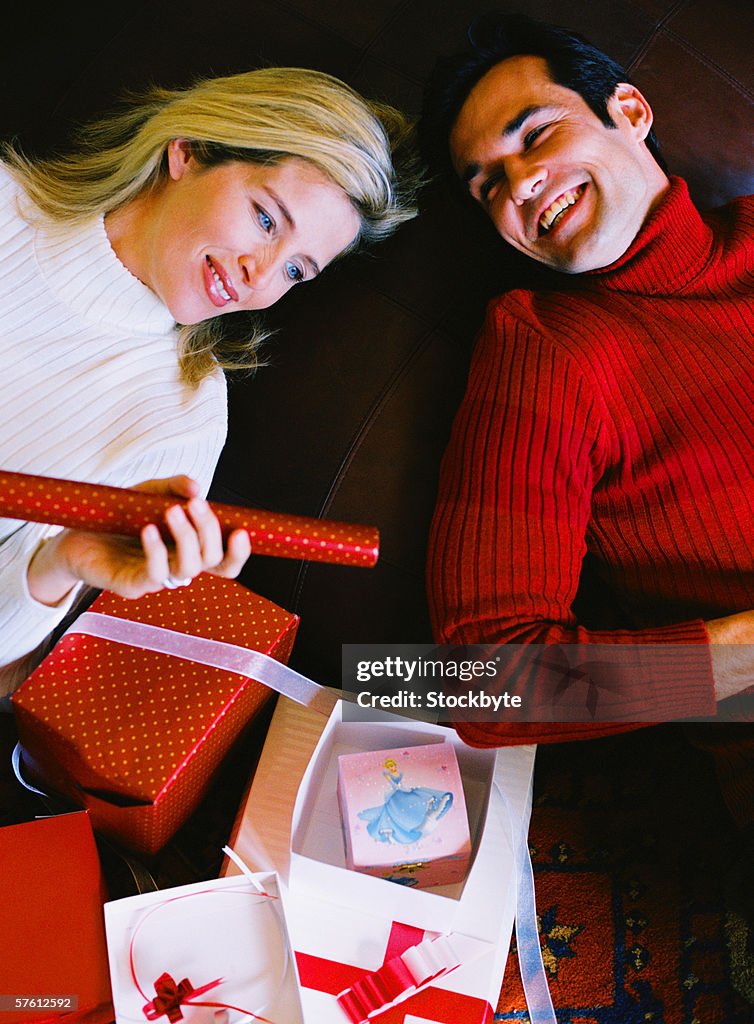Elevated view of a young woman lying down holding a roll of wrapping paper with a young man beside her