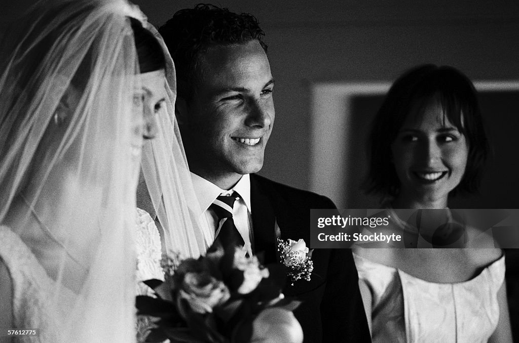 Close-up of the bride and groom with a bridesmaid standing beside them (black and white)