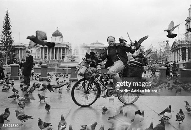 German round-the-world cyclist Heinz Stucke surrounded by pigeons in London's Trafalgar Square, 1977. The National Gallery is visible in the...