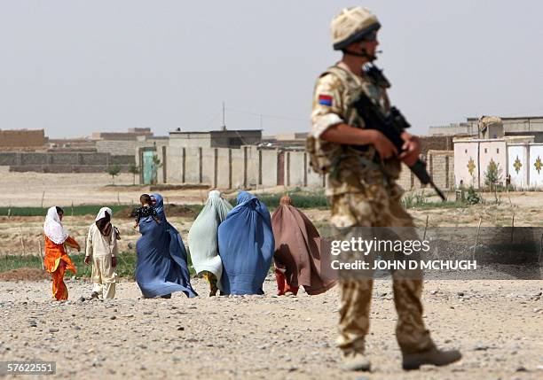 Lashkar Gah, AFGHANISTAN: A British soldier from 16 Air Assault Brigade holds his rifle as women in burkas walk past during a foot patrol in Lashkar...