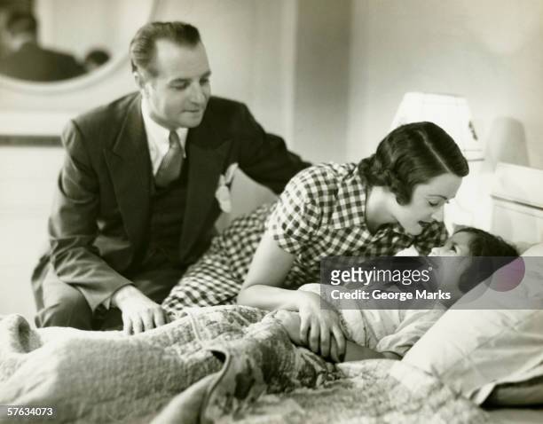 parents tucking daughter (6-7) into bed, (b&w) - 1940s bedroom stock pictures, royalty-free photos & images