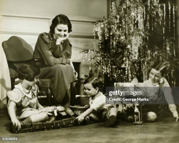 mother watching three children playing by christmas tree, (b&w) - miniature train stock pictures, royalty-free photos & images