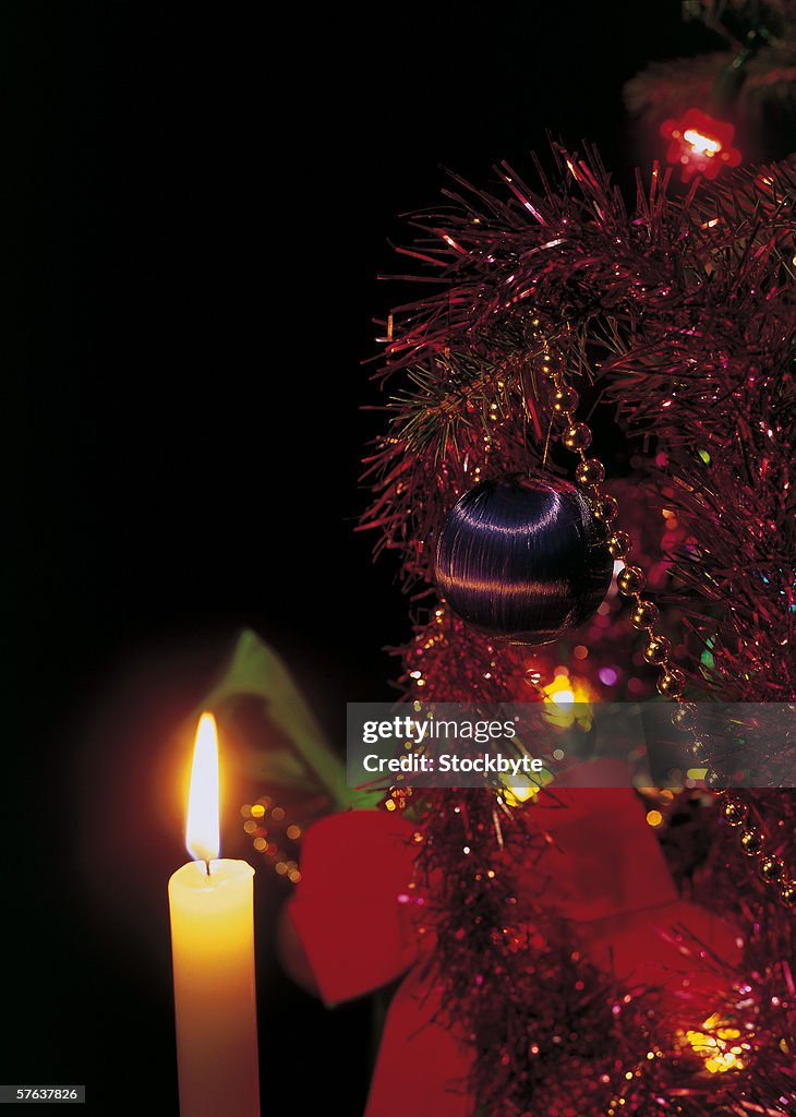 Close-up of a lit candle kept beside a decorated Christmas tree