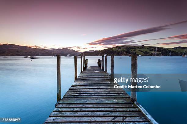 pink sunset over jetty and blue lake, new zealand - akaroa stock-fotos und bilder