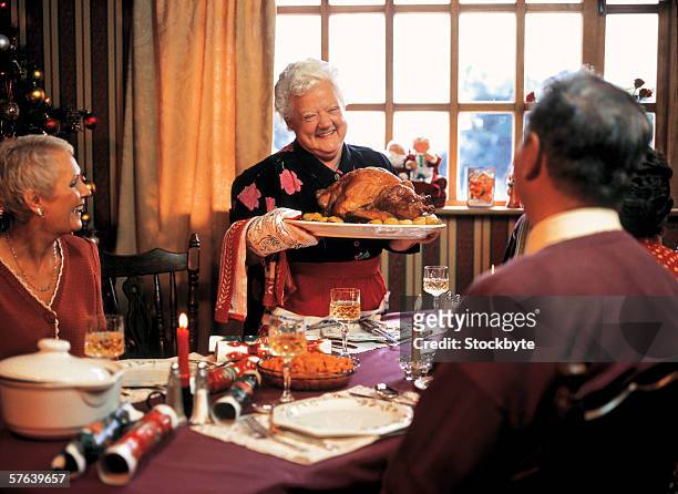 elderly woman bringing roast turkey to the dining table - cooked turkey white plate stockfoto's en -beelden