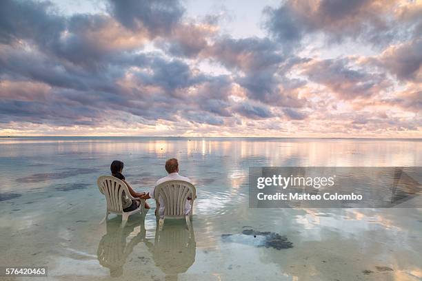 tourist couple admiring sunset on the sea aitutaki - couple sitting stock pictures, royalty-free photos & images