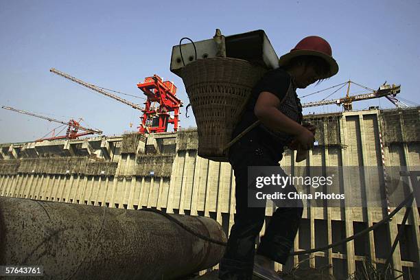 Woman carrying a back basket walks past the construction site of the Three Gorges Dam on May 17, 2006 in Yichang of Hubei Province, China. There are...