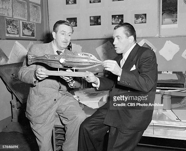 American film producer and animator Walt Disney sits on a workbench in a studio and shows television personality Ed Sullivan a submarine model for...