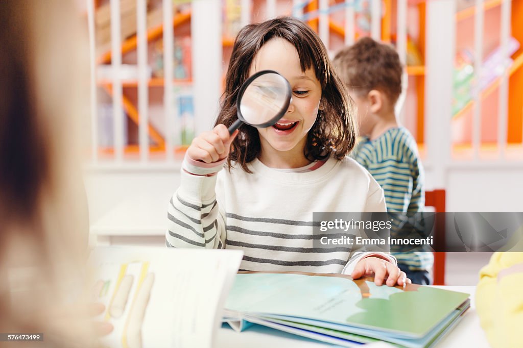 Girl smiling reading book with magnifying glass