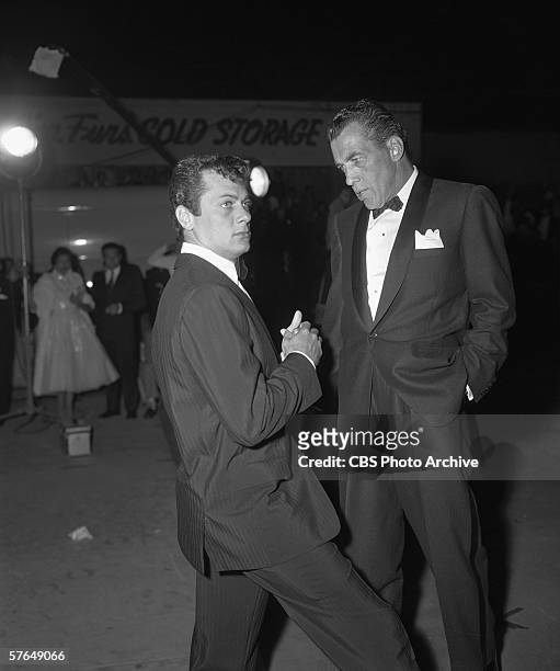 American television personality Ed Sullivan and actor Tony Curtis, both dressed in tuxedos, stand together and talk outside the Fox Wilshire Theater...