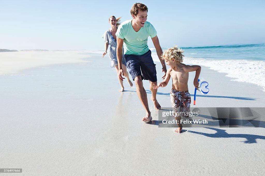 Parents with son (5-6) running on beach