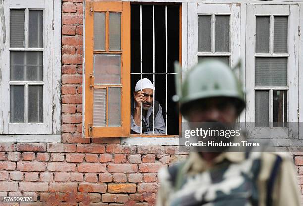 Kashmiri man looks out of a window as an paramilitary soldier stands guard during a curfew on July 15, 2016 in Srinagar, India. Curfew imposed in...