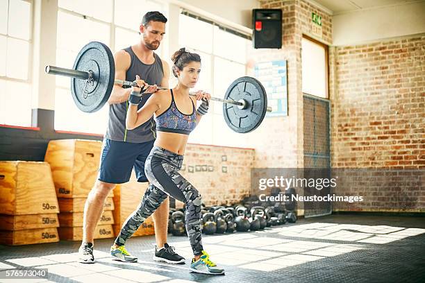 frau heben langhantel, während personal trainer hilft ihr in gy - weight lifting stock-fotos und bilder