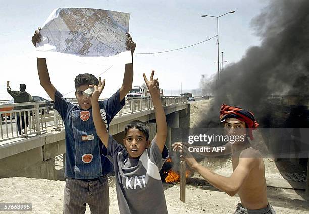 Iraqi youths flash the "V" sign at the site where a British military vehicle is buring in the southern city of Basra, 20 May 2006. Two British...