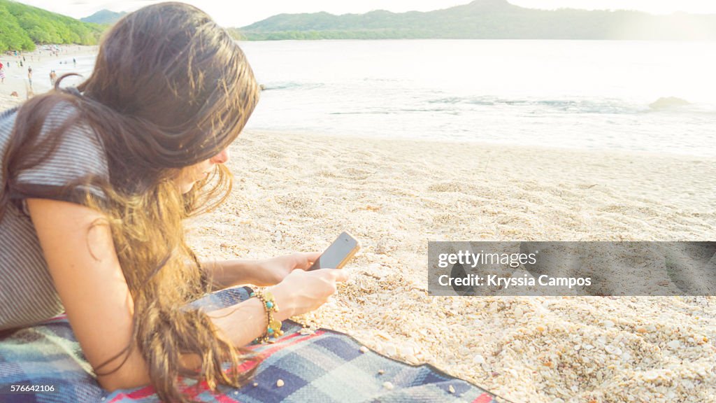 Side view of a woman texting in a smart phone on the beach with the sea in the background