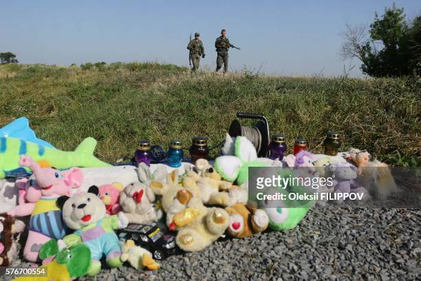 Pro-Russia armed rebels walk near stuffed animals and candles left at the site of the MH17 flight crash near Grabove village, Donetsk region, on July...