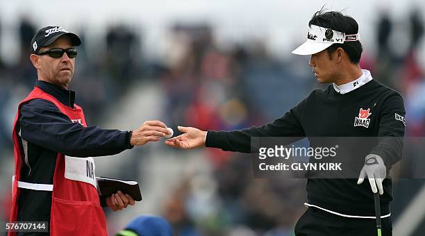 Caddie Kenny Harns hands a ball to US golfer Kevin Na on the 6th tee during his final round on day four of the 2016 British Open Golf Championship at...
