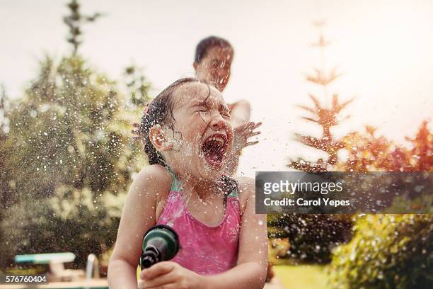 girl (4-5) in bathing suit sprayed with water hose. - spensieratezza foto e immagini stock