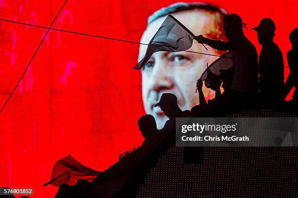 People wave Turkish flags in front of an electronic billboard displaying the face of President Recep Tayyip Erdogan at a rally on the streets of...