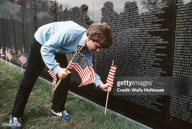 Boy places flags in the ground before each of the memorial panels in preparation of the opening of the Vietnam Veterans Memorial in Washington, DC,...