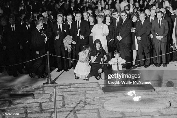 Jackie Kennedy and children Caroline and John kneel at the gravesite of husband and father President John Kennedy. Caroline prepares to place a...