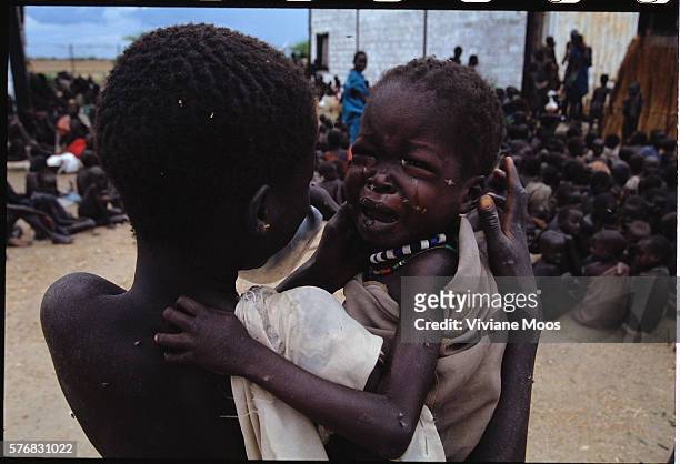 An emaciated child cries as he awaits a meal at a feeding center in Kongor, Sudan. Civil war and widespread famine have ravaged Sudan for decades,...