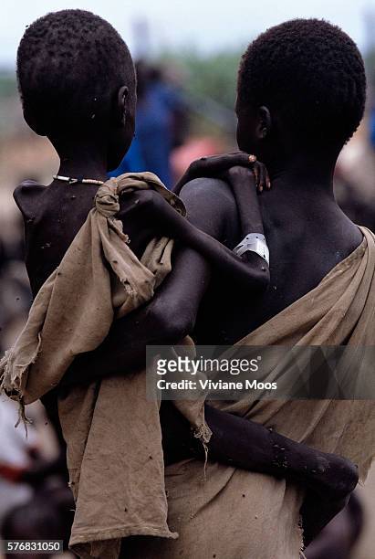 An emaciated child is held in the arms of a family member as the two await a meal at a feeding center in Kongor, Sudan. Civil war and widespread...