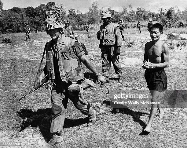 Marine leads a Vietcong suspect during a Battalion operation. The soldier carries what appears to be a M-14 and sweats through his flak jacket and...