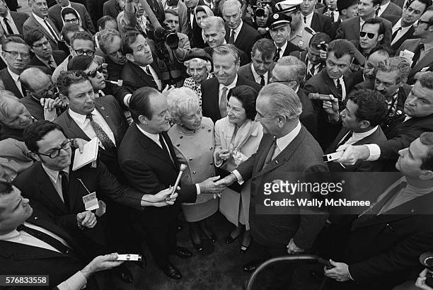 Reporters crowd around Hubert Humphrey, who is accompanied by his wife Muriel, as he shakes hands with President Lyndon B. Johnson, who stands with...