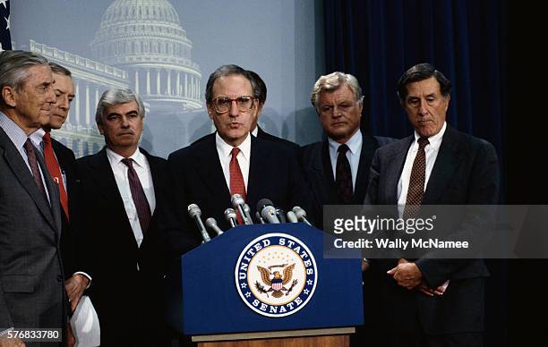 Senators Lloyd Bentsen, Orrin Hatch, Christopher Dodd, George Mitchell, Edward Kennedy, and John H. Chafee surround a podium.