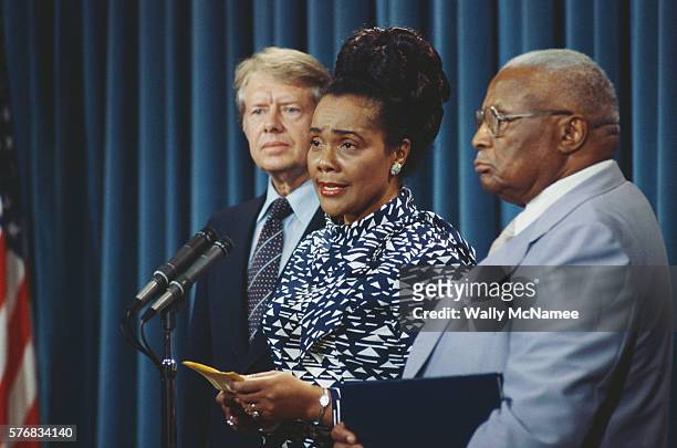 Coretta Scott King speaks at a microphone, flanked by President Jimmy Carter and her father-in-law Martin Luther King, Sr.
