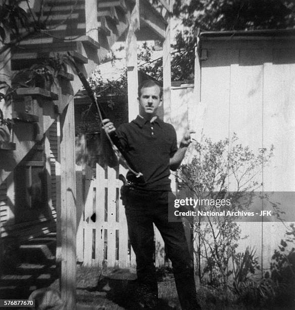 Lee Harvey Oswald holds a Mannlicher-Carcano rifle and a newspaper in a backyard. This photograph is one of the controversial backyard photos used in...