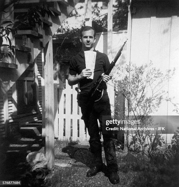 Lee Harvey Oswald holds a Mannlicher-Carcano rifle and newspapers in a backyard. This photograph is one of the controversial backyard photos used in...