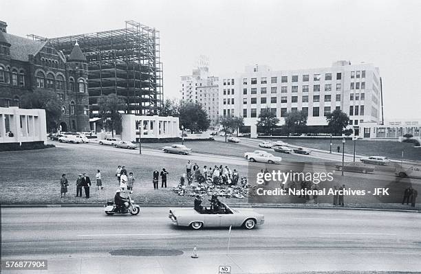 Reenactment of the Kennedy assassination occurs at Dealey Plaza in Dallas, Texas. Mourners stand beyond near flowers and wreaths left in honor of the...