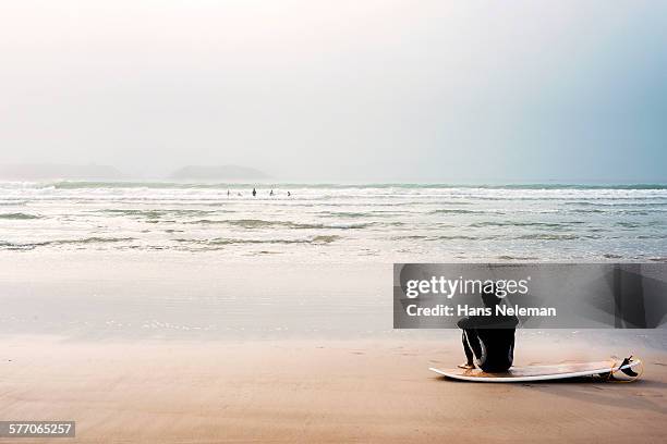man sitting on beach by surfboard - essaouira stock-fotos und bilder