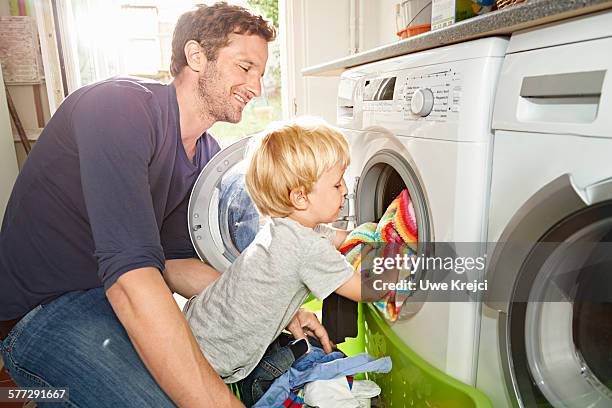 father and son loading washing machine - domestic chores photos et images de collection